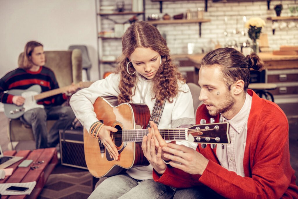 Tutor teaching teenagers to play the guitar